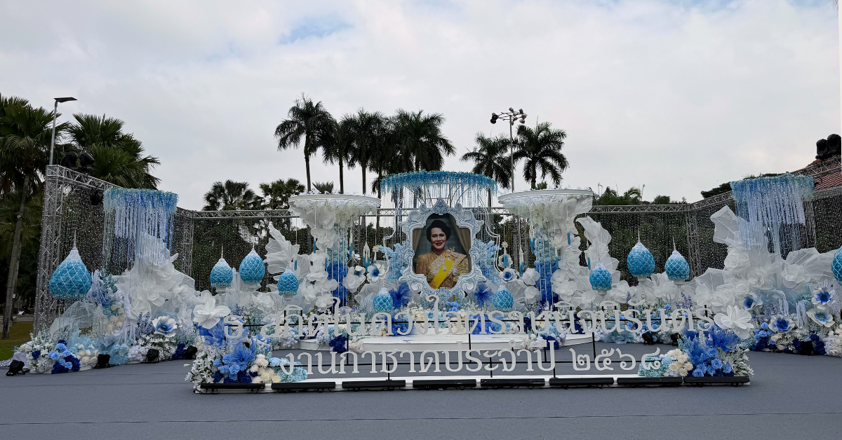การออกแบบเวทีพิธีการงานกาชาดประจำปี 2568 ใช้องค์ประกอบดอกไม้และโครงสร้างสีฟ้า–ขาว สื่อถึงความสุภาพและเป็นทางการ