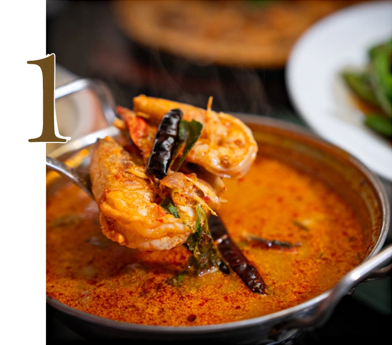 Close-up of authentic Tom Yum Kung spicy Thai soup with large prawns, mushrooms, and fresh herbs in a traditional metal pot from Hua Seng Hong restaurant.