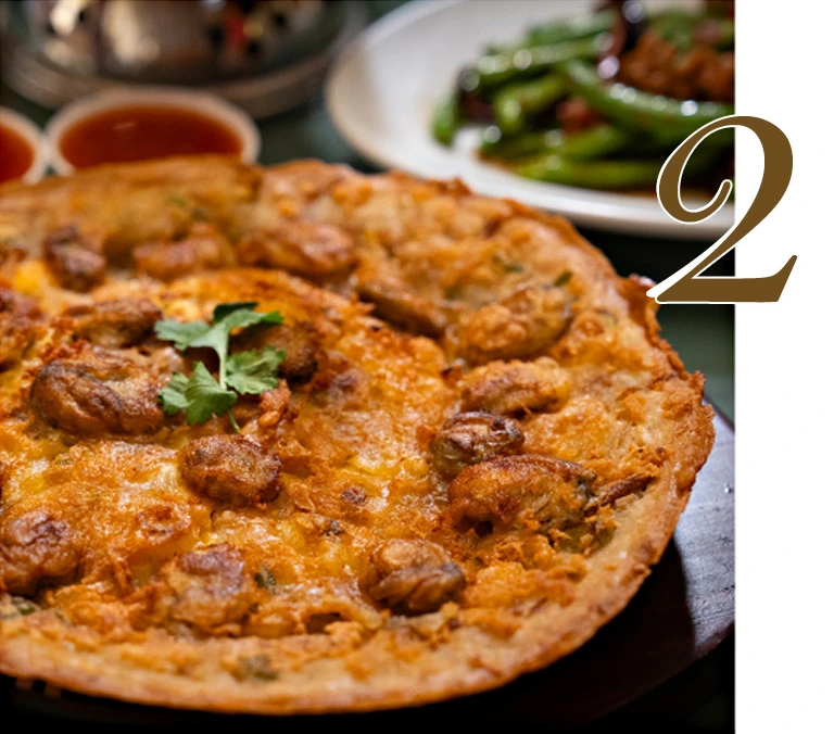 Sizzling Fried Crispy Oysters with Egg on a hot plate, featuring golden-brown crispy batter, fresh plump oysters, and garnish, a signature Thai-Chinese dish at Hua Seng Hong.