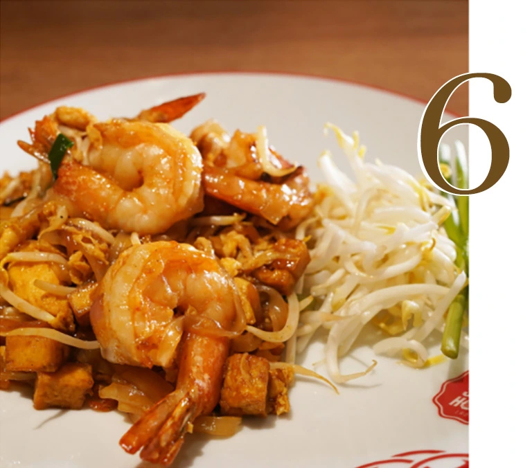 A delicious plate of authentic Pad Thai Goong featuring stir-fried rice noodles, large fresh shrimps, tofu, and a side of fresh bean sprouts and chives at Hua Seng Hong restaurant.