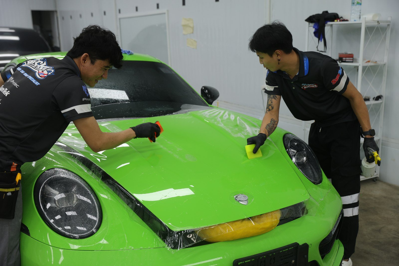 ช่างติดฟิล์มใสบริเวณด้านหน้ารถ Porsche สีเขียว