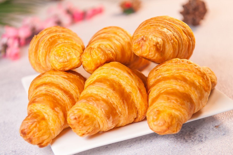 A croissant is a crescent-shaped, laminated pastry made by folding butter into dough multiple times to create dozens of delicate layers. When baked, those layers puff up into a golden, crispy shell with a light, airy interior.