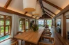 The dining table beneath the vaulted timber ceiling, open on both sides to the pool and garden
