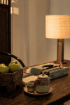 A table lamp, woven basket and a bowl of green fruit on a timber console