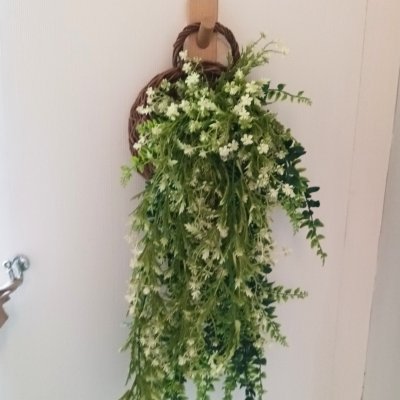 ดอกไม้เลื้อยปลอมสีขาวในตะกร้าสานแขวนผนัง Artificial white climbing flowers in a woven basket.