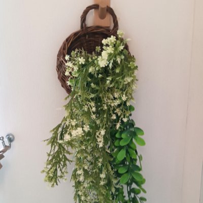ดอกไม้เลื้อยปลอมสีขาวในตะกร้าสานแขวนผนัง Artificial white climbing flowers in a woven basket.