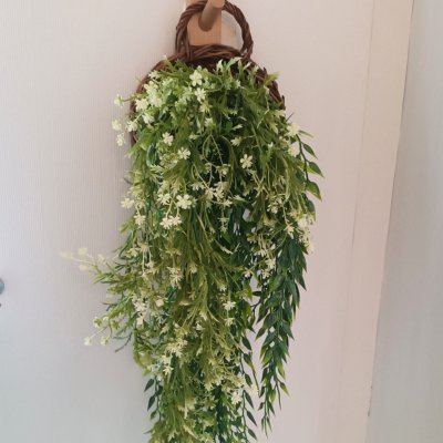 ดอกไม้เลื้อยปลอมสีขาวในตะกร้าสานแขวนผนัง Artificial white climbing flowers in a woven basket.