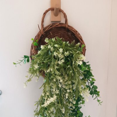 ดอกไม้เลื้อยปลอมสีขาวในตะกร้าสานแขวนผนัง Artificial white climbing flowers in a woven basket.