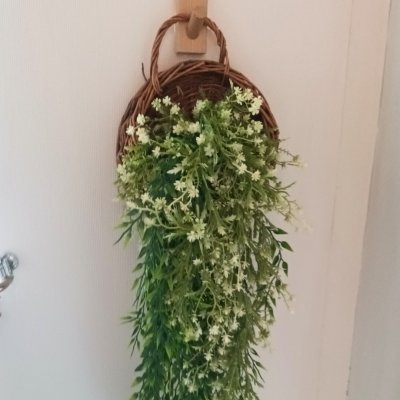 ดอกไม้เลื้อยปลอมสีขาวในตะกร้าสานแขวนผนัง Artificial white climbing flowers in a woven basket.