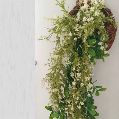 ดอกไม้เลื้อยปลอมสีขาวในตะกร้าสานแขวนผนัง Artificial white climbing flowers in a woven basket.