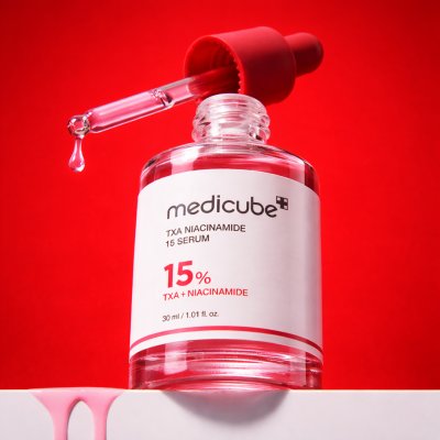 เนื้อเซรั่มใสของ Medicube TXA Niacinamide 15 Serum บนดรอปเปอร์ แสดงความบางเบา ซึมง่าย พร้อมพื้นหลังสีแดงสื่อถึงผิวโกลว์กระจ่างใส