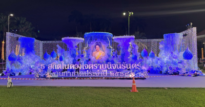 เวทีพิธีการงานกาชาดประจำปี 2568 ในยามค่ำคืน  ใช้องค์ประกอบดอกไม้และโครงสร้างสีฟ้า–ขาว สื่อถึงความสุภาพและเป็นทางการ