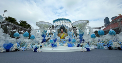 การออกแบบเวทีพิธีการงานกาชาดประจำปี 2568 ใช้องค์ประกอบดอกไม้และโครงสร้างสีฟ้า–ขาว สื่อถึงความสุภาพและเป็นทางการ