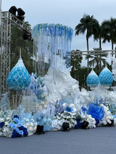 ซุ้มพิธีการงานกาชาดประจำปี 2568 ตกแต่งด้วยดอกไม้โทนสีฟ้าและขาว จัดวางอย่างสุภาพตามรูปแบบพิธีการกลางแจ้ง