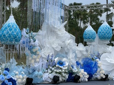 รายละเอียดงานตกแต่งซุ้มพิธีการด้วยดอกไม้โทนสีฟ้าและขาว สำหรับงานกาชาดประจำปี จัดวางตามลำดับพิธีการ