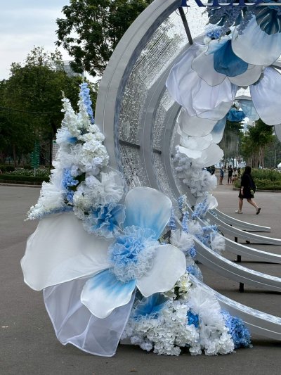 การออกแบบเวทีพิธีการงานกาชาดประจำปี 2568 ใช้องค์ประกอบดอกไม้และโครงสร้างสีฟ้า–ขาว สื่อถึงความสุภาพและเป็นทางการ