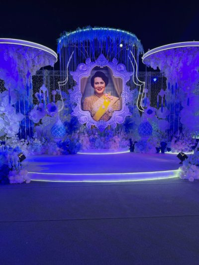 พระบรมฉาลาลักษณ์โดดเด่นในยามค่ำคืน  ดุจศูนย์รวมดวงใจคนไทยทั้งชาติพิธีการงานกาชาดประจำปี 2568 ใช้องค์ประกอบดอกไม้และโครงสร้างสีฟ้า–ขาว สื่อถึงความสุภาพและเป็นทางการ