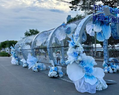 การออกแบบเวทีพิธีการงานกาชาดประจำปี 2568 ใช้องค์ประกอบดอกไม้และโครงสร้างสีฟ้า–ขาว สื่อถึงความสุภาพและเป็นทางการ