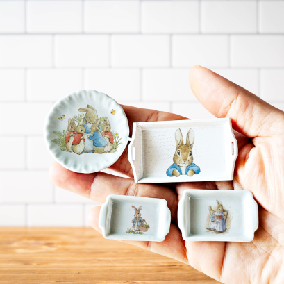 Set of four miniature Peter Rabbit-themed ceramic dishes, featuring a plate and trays, perfect for dollhouse decor or collectible gifts.