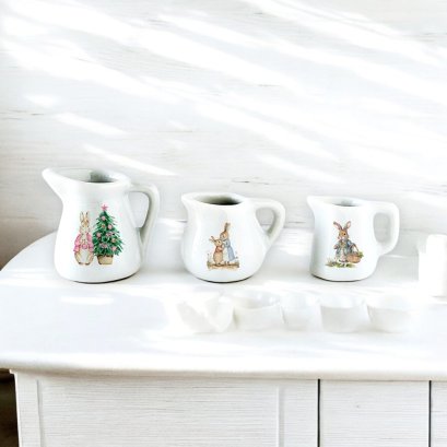 Set of three miniature ceramic pitchers featuring Peter Rabbit designs, perfect for dollhouse kitchen decor or 1:12 scale collections.