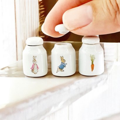 Set of three miniature ceramic storage jars featuring Peter Rabbit designs, perfect for dollhouse kitchen decor or 1:12 scale collections.