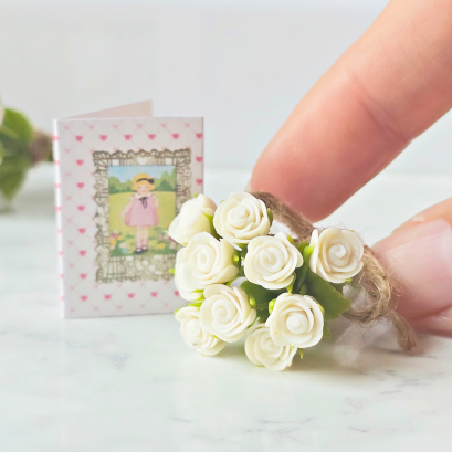 Miniature white rose bouquet tied with twine and accompanied by a tiny vintage-style gift card, perfect for dollhouse decor or special gifts.