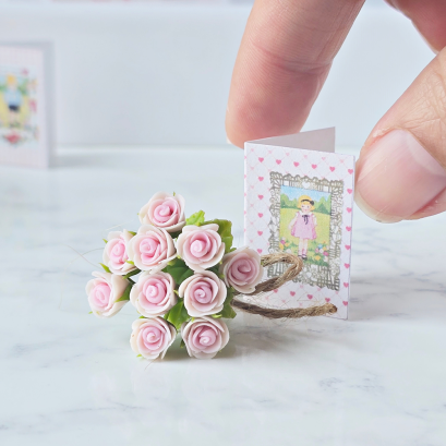 Miniature pink rose bouquet tied with twine and accompanied by a tiny vintage-style gift card, perfect for dollhouse decor or special gifts.