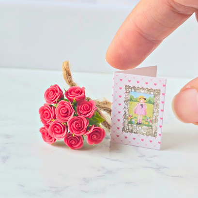 Miniature red rose bouquet tied with twine and accompanied by a tiny vintage-style gift card, perfect for dollhouse decor or special gifts.