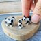 Three miniature ceramic dog figurines in 1:12 scale lined up next to a ruler, displaying their small size and intricate craftsmanship, ideal for collectors.