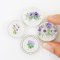 Miniature ceramic decorative plates featuring intricate purple floral designs, perfect for dollhouse kitchens, collectibles, and elegant tiny decor.