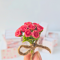 Miniature red rose bouquet tied with twine and accompanied by a tiny vintage-style gift card, perfect for dollhouse decor or special gifts.